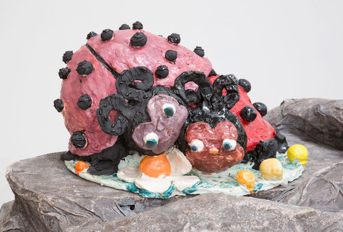 Sculpture of two ladybugs with noses and large eyes laying on top of each other