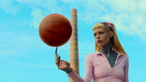 A heavily tattooed woman spins a basketball on a long, witch-like finger