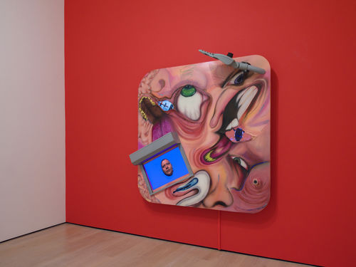 Square multi-media work with distorted images of faces and video screens, on a bright red wall