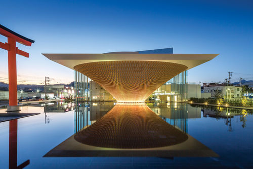 A glowing building in the shape of an inverted pyramid, with a reflecting pool in front of it