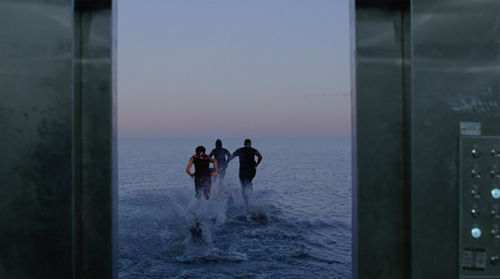 Three figures, viewed from behind, running into the ocean
