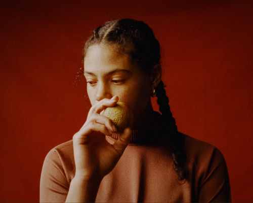A person with braids holds a fruit infront of their face