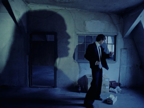 A man in a suit, dwarfed by the shadow of a woman's head