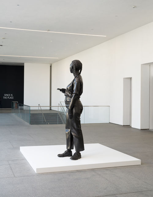 Larger-than-life bronze sculpture of a Black woman looking down at her cell phone