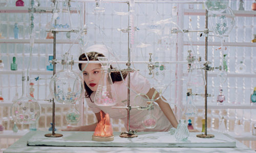 Olivia Rodrigo looks intently at a glass beaker while wearing a vintage nurse outfit