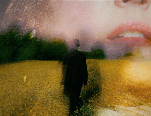 A blurry figure of a man stands in the middle, with a blurry close up of a woman's lower face makes up the background