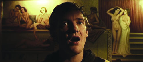 A man standing in front of a painted background appears to be singing