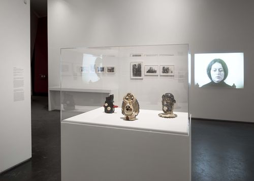 Feminisms gallery. In vitrine, from left to right: Tecla Tofano, Medio de reproducción visual (Visual reproduction medium), 1973, En via de liberación (On the way to liberation), 1975, and Sra. Mascara de Cutis (Mrs. Skin Mask), 1977; projected on wall: Patricia Restrepo, Por la mañana (In the Morning), 1980. Installation view at Brooklyn Museum, New York
