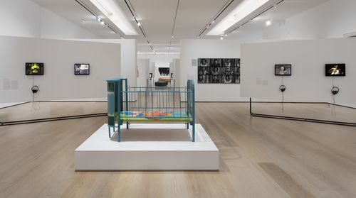 Social Places gallery. Foreground: Beatriz González, Canción de cuna (Lullaby), 1970; monitors, from left to right: Diamela Eltit, Zonas de dolor II (Zones of Pain II), 1982, Letícia Parente, Tarefa 1 (Chore 1), 1982, Poli Marichal, Los espejismos de Mandrágora Luna (Mandrágora Luna's phantoms), 1986, and Ximena Cuevas, Las tres muertes de Lupe (The Three Deaths of Lupe), 1984. Installation view at the Hammer Museum, Los Angeles
