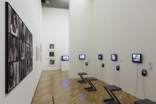 Lugares sociais (Social Places) gallery. Foreground, at left: Claudia Andujar, works from the series Marcados (Marked), 1981–83; right wall, on monitors, from left to right: Diamela Eltit, Zonas de dolor II (Zones of Pain II), 1982, Narcisa Hirsch, Marabunta (Swarm), 1967, Patssi Valdez, Hot Pink, 1980, and Poli Marichal, Los espejismos de Mandrágora Luna (Mandrágora Luna's phantoms), 1986. Installation view at Pinacoteca de São Paulo
