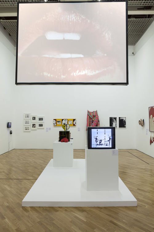 O erótico (The Erotic)/Performance do corpo (Performing the Body) gallery. Projected above: Lygia Pape, Eat Me, 1975; on pedestals, from left to right: Teresinha Soares, Caixa de fazer amor (Lovemaking Box), 1967, and Analívia Cordeiro, M 3x3, 1973. Installation view at Pinacoteca de São Paulo
