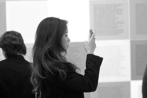 A guest takes a photo in front of Jenny Holzer, "Inflammatory Essays," 1979–81, during the opening of "Take It or Leave It," Hammer Museum, Los Angeles, February 8, 2014