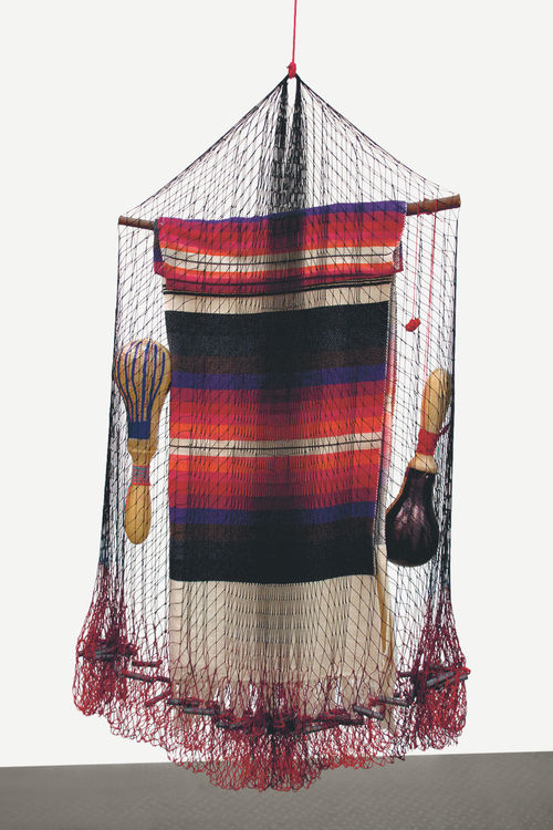 Carolina Caycedo, Cosmotarraya Yaqui, 2016. Hand-dyed artisanal fishing net, led weights, wood stick, cotton poncho, leather maracas, dry chile pepper. 35 7/16 x 21 21/32 x 3 15/16 in. (90 x 55 x 10 cm). Image courtesy the artist.