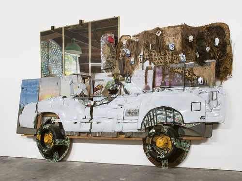 Aaron Fowler, El Camino, 2017. Acrylic paint, enamel paint, car parts, hair weave, mirrors, CDs, fans, fitted cap, tires, poker tables, speakers, digital printout, and concrete cement on conference tables. 132 x 168 x 48 in. (335.3 x 426.7 x 121.9 cm). Courtesy the artist.
