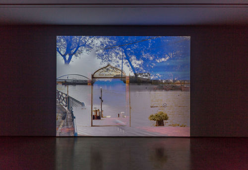 Projected video of superimposed images of a gate, a bridge, trees, and more