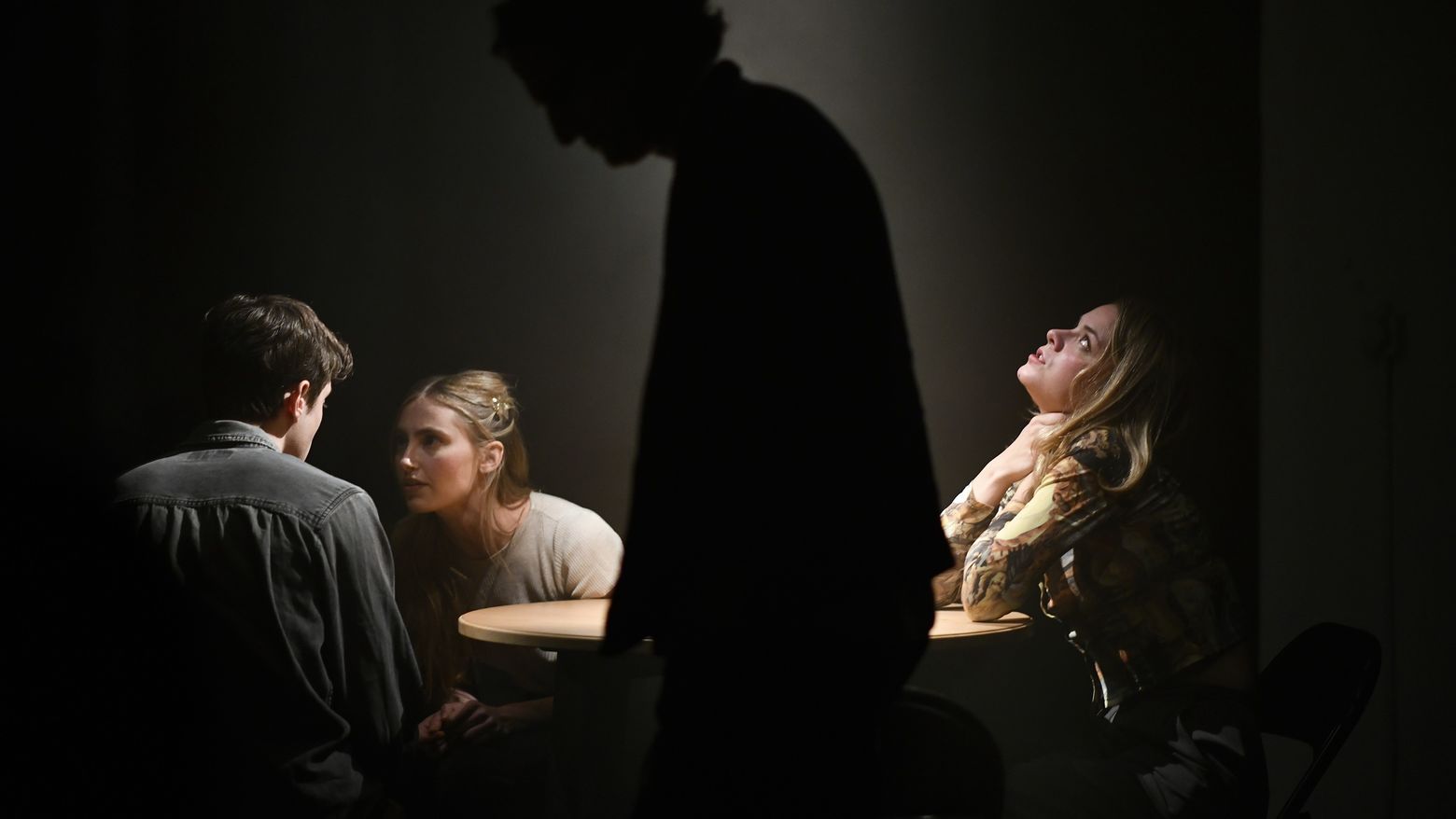 Three people at a table with the silhouette of a figure in front