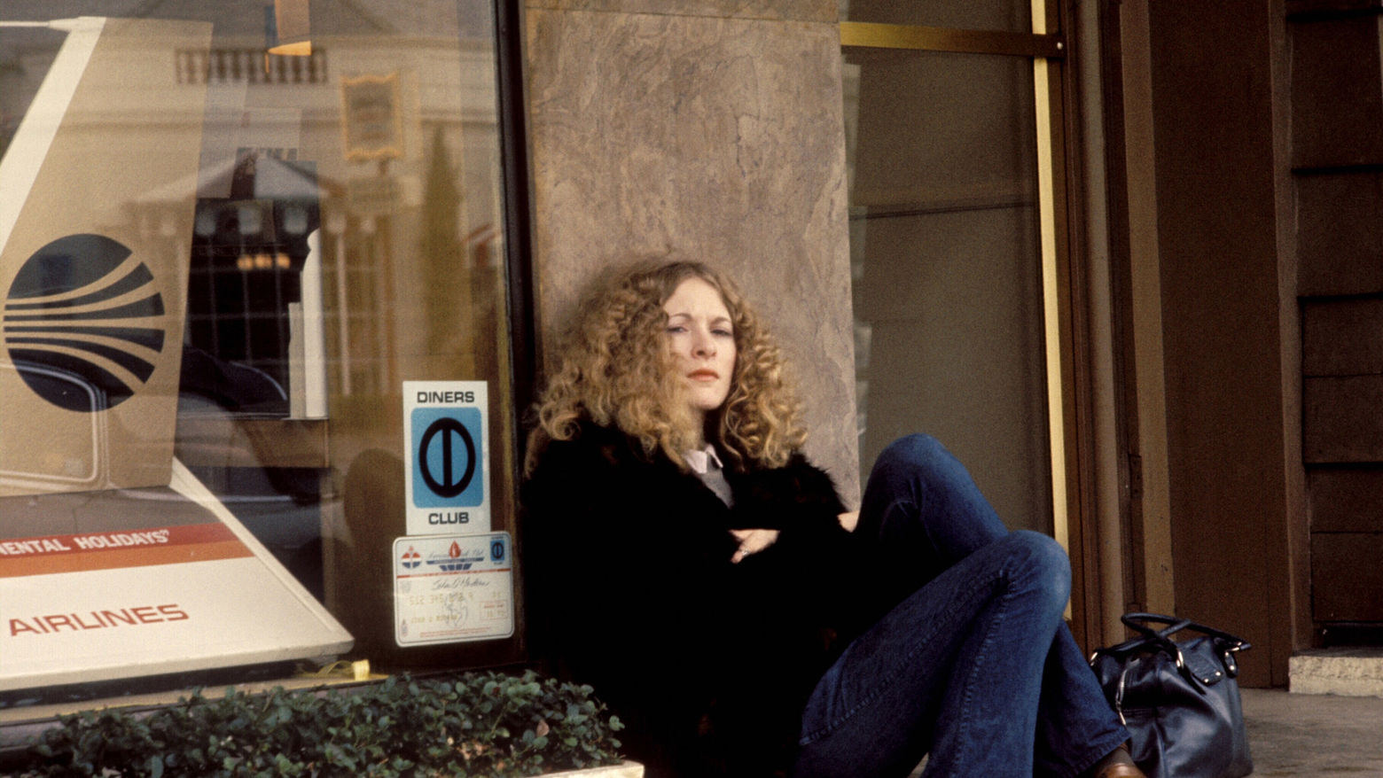 Still from the film Dusty and Sweets McGee (1971) showing a woman seated on the sidewalk, leaning against a building
