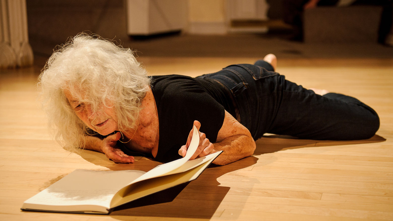 A woman lies on the ground, looking into an open book