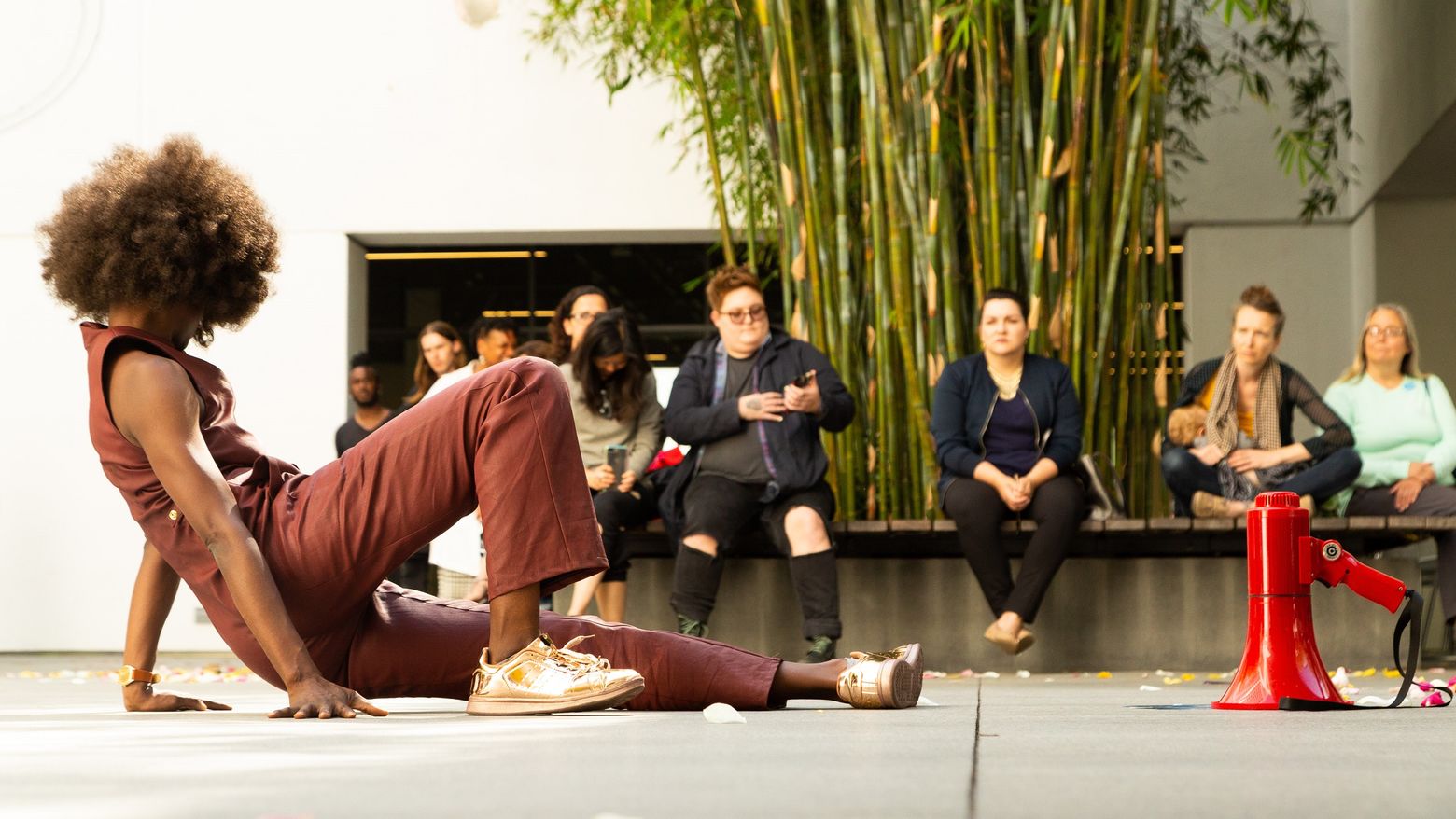 An artist reclines on the ground next to a red megaphone while the audience watches