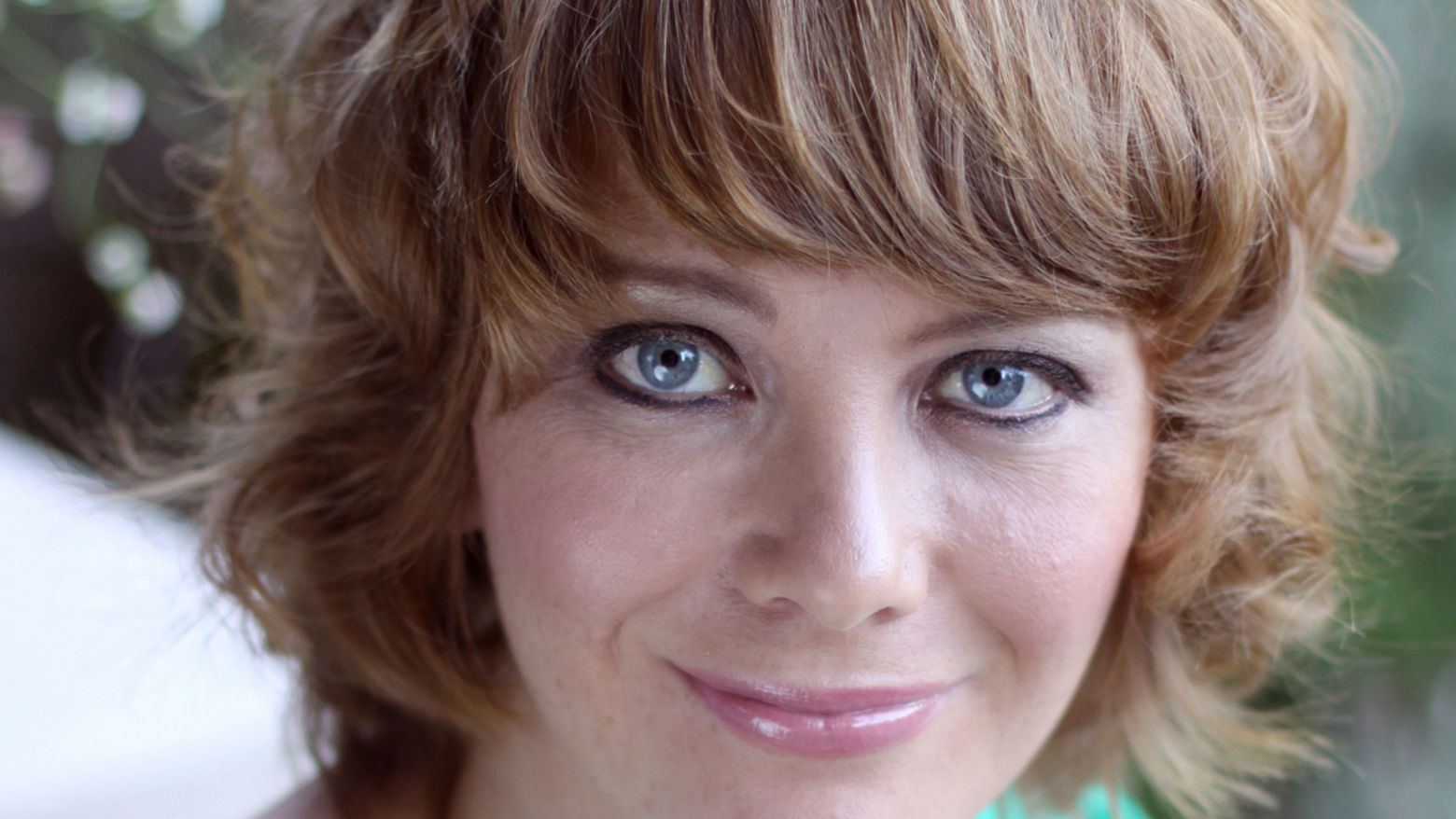Photograph of a woman facing the camera, smiling, wearing a teal shirt