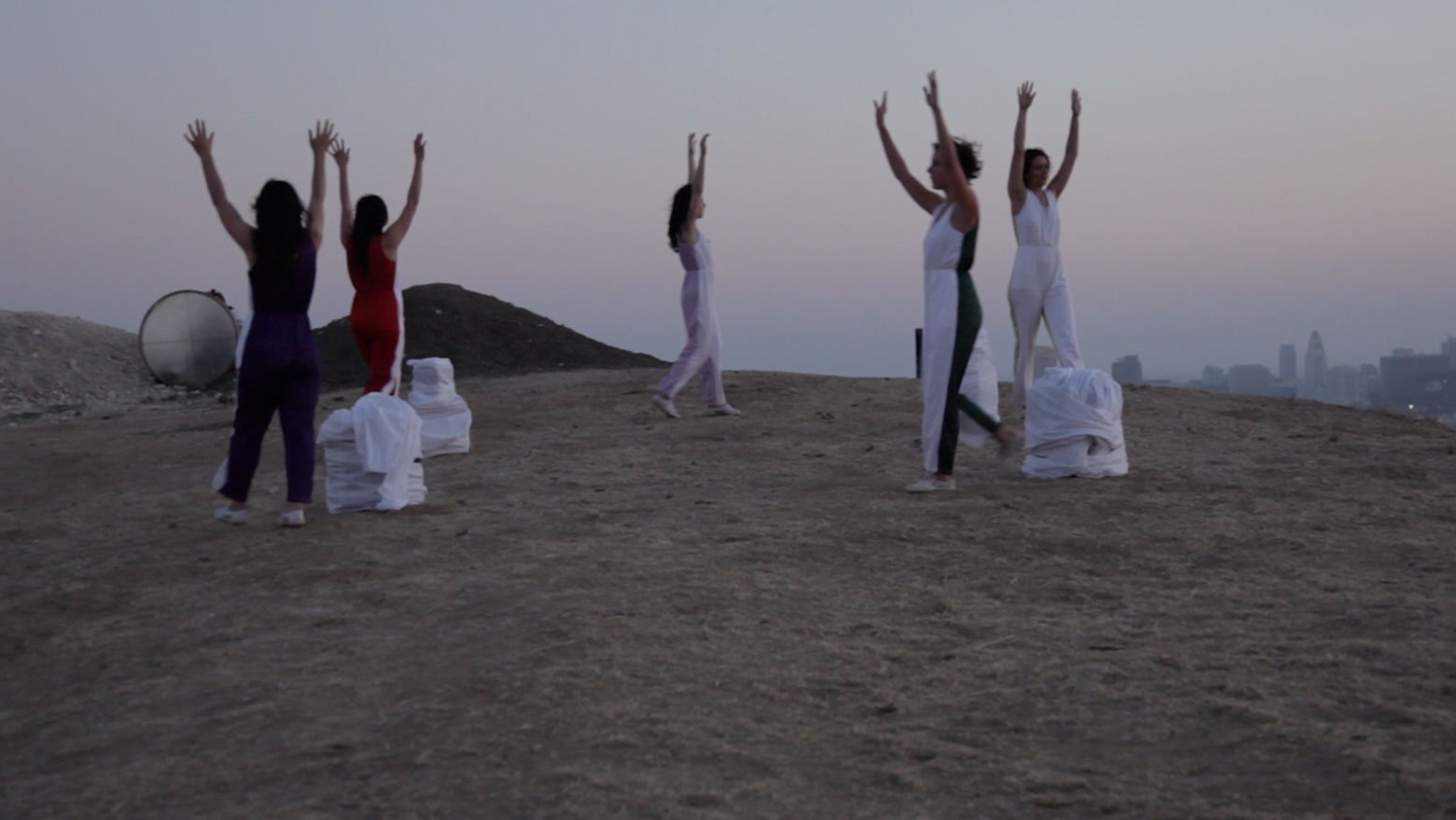 Five figures stand with their arms up, walking across a hill
