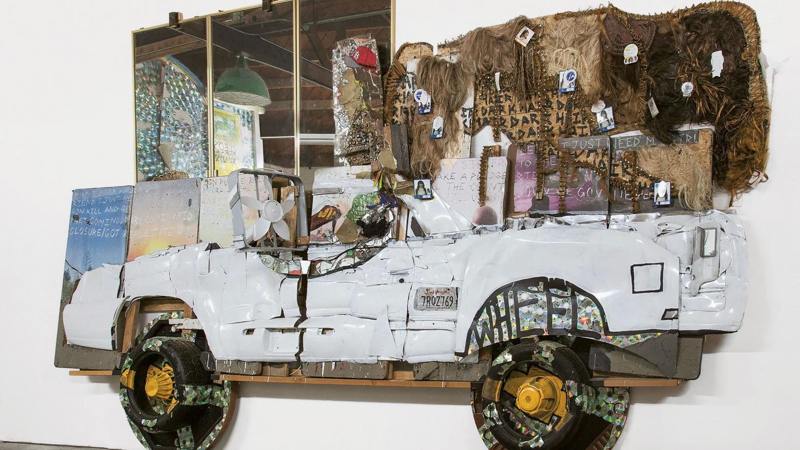 Aaron Fowler, El Camino, 2017. Acrylic paint, enamel paint, car parts, hair weave, mirrors, CDs, fans, fitted cap, tires, poker tables, speakers, digital printout, and concrete cement on conference tables. 132 x 168 x 48 in. (335.3 x 426.7 x 121.9 cm). Courtesy the artist.