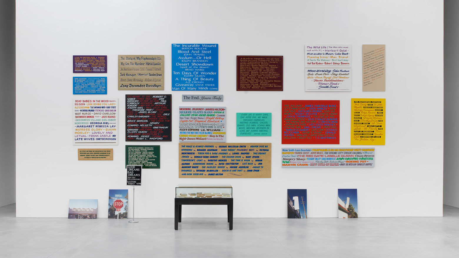 Allen Ruppersberg, Good Dreams, Bad Dreams (What Was Sub-Literature?), 1996. Mixed-media installation with nineteen hand-painted signs, stanchion sign, four color photographs, forty books from the artist’s collection. Collection Aïshti Foundation, Beirut; Installation view of the exhibition Good Dreams, Bad Dreams,: American Mythologies; photo: Guillaume Ziccarelli.