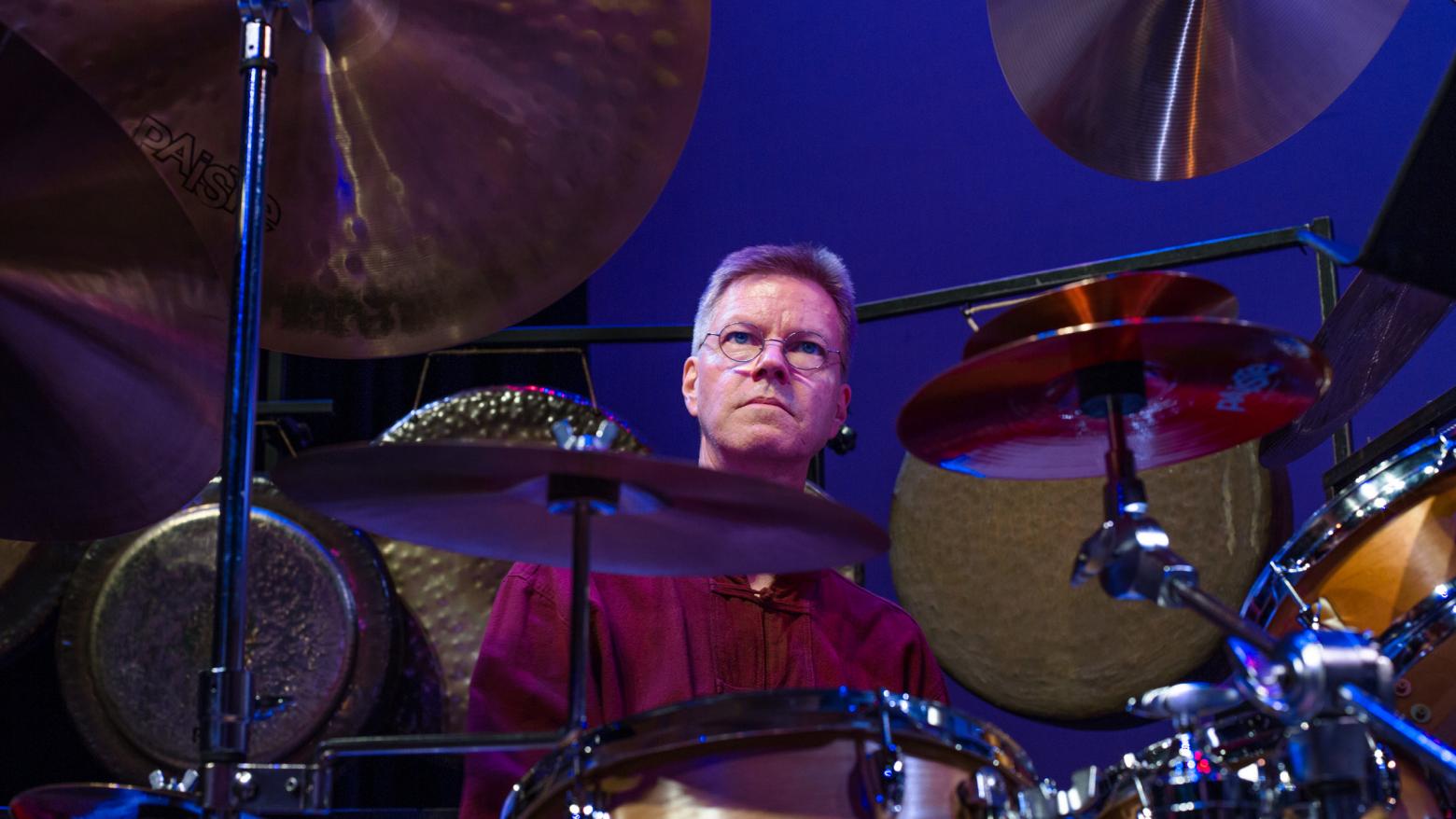 Alex Cline sits behind a set of drums and cymbals.