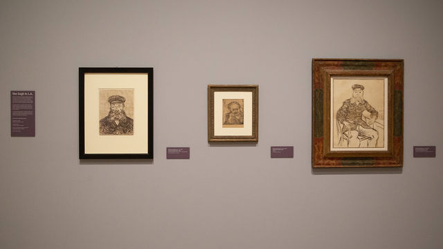 A gallery wall with three Van Gogh works on paper hung on it, and didactic labels. The wall is painted a neutral brown grey and the prints are all dark brown lines on parchment colored paper.