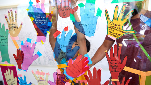 A child presses his hands to a glass covered in paper hand cut-outs