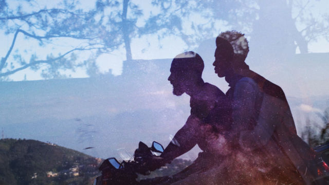 A silhouette of two people riding on a horse is set against a background of a dusk sky with shadows of trees.