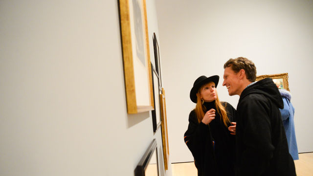 Two people look at paintings on a wall