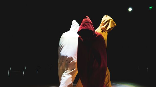 Three figures in hoods walk around a stage