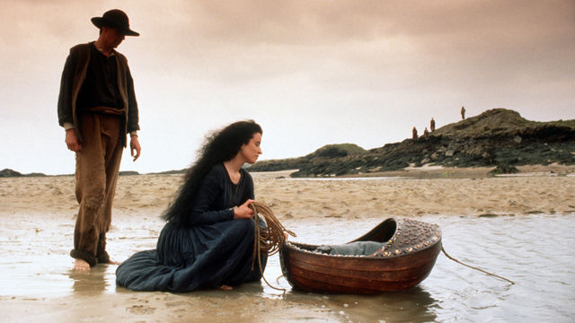 Still from the film The Secret of Roan Inish (1994) showing a woman crouching in the water, over a floating bassinet , with a man standing nearby