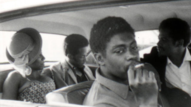 Still from the film Several Friends (1969) showing four people in a car with the man in the foreground smoking a cigarette