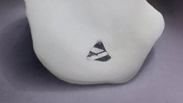 A white stone with a small black-and-white cutout on a grey background