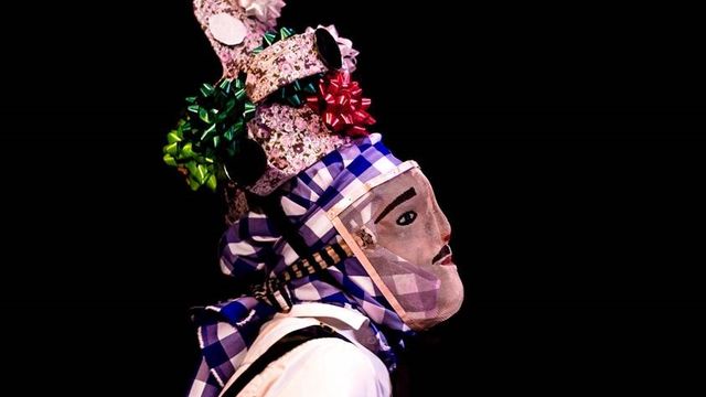 A masked dancer with tall headdress viewed in profile