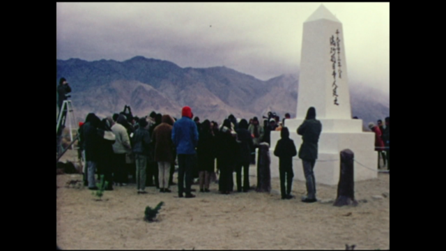 Still from the film Pilgrimage showing a group gathered around a monument built at a former WWII concentration camp for Japanese Americans