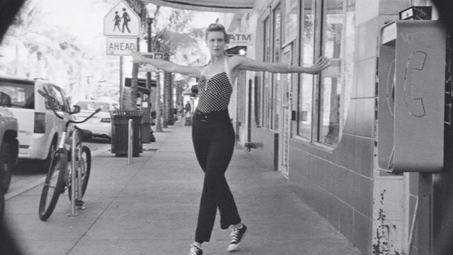 A black-and-white shot of a woman dancing on a sidewalk