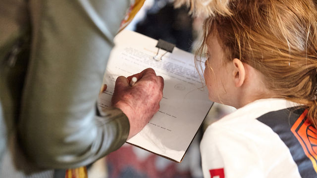 A young girl looks at a piece of paper while someone writes on it