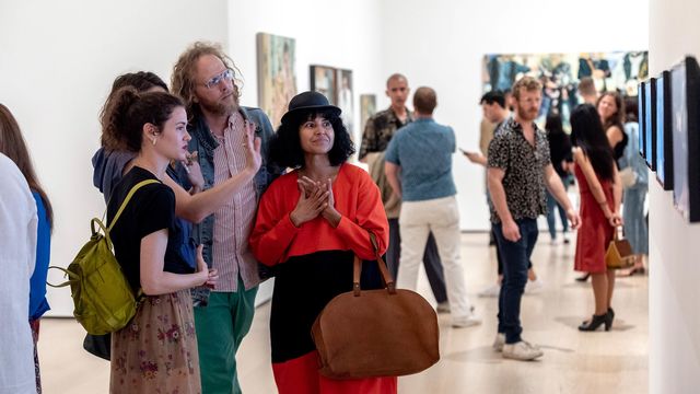 Four people stand in a gallery looking at works of art and talking together.