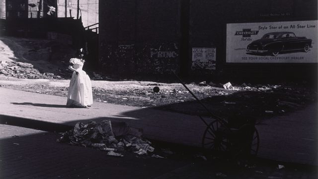 A woman in a white dress walks down a street