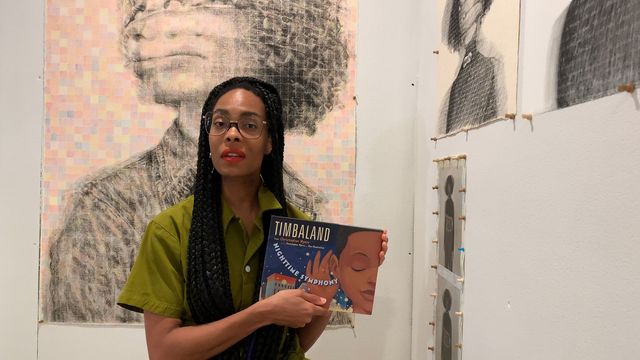 A woman sits before artworks holding a book