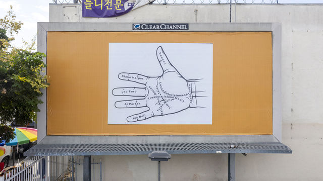 Photo of a billboard against a white building, with a square image of a palmistry diagram in black and white  pasted on top of a gold backgrounf.