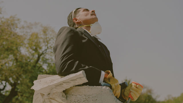 A man with a construction mask around his chin stands in a concrete tube, looking up at the sky