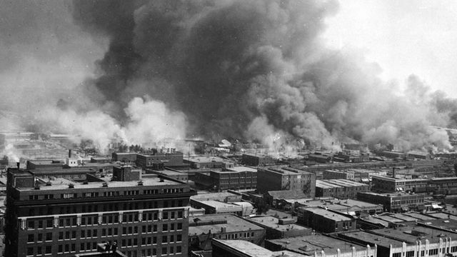 Black and white aerial photo of huge billows of smoke rising from Tulsa, Oklahoma, as it burned from the result of the 1921 Tulsa Race Massacre.