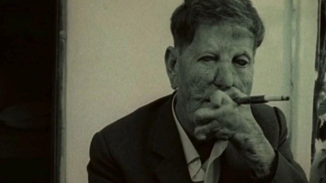 Still from the film 1972 film "L'Ordre," showing a man with leprosy in a suit smoking a cigarette..