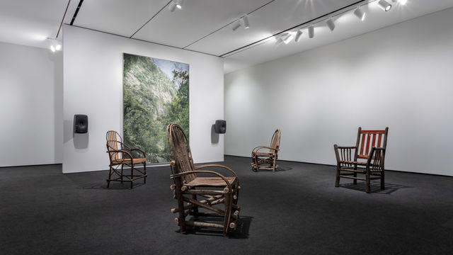 Four wooden chairs sit in the same room as David Hartt's painting