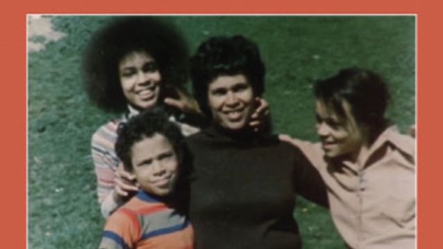 Mother with three children smiling on grass field.