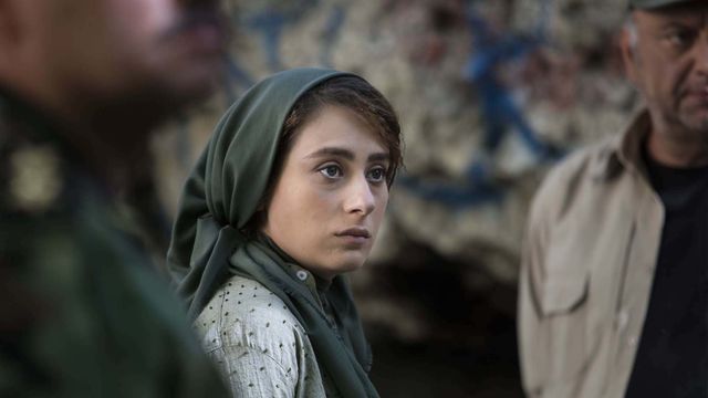 A woman wearing a hijab staring, located between two blurred men.